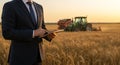 Man in suit uses tablet in wheat field with tractors Royalty Free Stock Photo