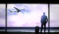 Man with suitcase looking out at the airport window while waiting for flight departure Royalty Free Stock Photo