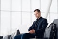 Man with suitcase sitting in airport waiting area while listening music using airpods Royalty Free Stock Photo