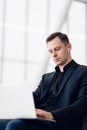 Man with suitcase sitting in airport waiting area while listening music using airpods Royalty Free Stock Photo