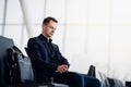 Man with suitcase sitting in airport waiting area while listening music using airpods Royalty Free Stock Photo