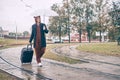 Man with a suitcase is walking along the road. guy holds an umbrella in the rain Royalty Free Stock Photo