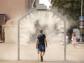 A man in summer clothes goes through the frame of a refreshing street shower. Use fine water dust during the hot season