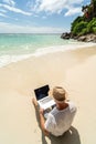 Man in the summer hat , a businessman, digital nomad working with laptop on the sandy beach. Freelancer. Tropics Royalty Free Stock Photo