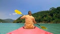 Man with sunglasses and hat rows pink plastic canoe along sea ag Royalty Free Stock Photo