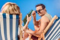 Man in sunglasses looking at beer bottle in female hand while sitting in beach chair Royalty Free Stock Photo