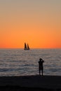 Man saluting sunset with sailboat on the horizon