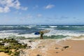 a man surfing at Sandy Beach with vast blue ocean water, rocks covered in lush green algae, crashing waves, blue sky and clouds Royalty Free Stock Photo