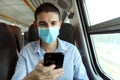 Man with surgical mask using smart phone app on public transport. Train passenger with protective mask traveling sitting in