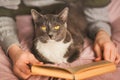 A man lies with his gray cat on a bed with a pink blanket and reads an interesting old book. Rest at home. Spending time with your