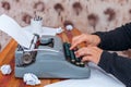 The man in a sweater typing on an old-fashioned typewriter. On the table are glasses and there is a mug