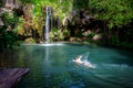 A man swims in a lagoon near a waterfall. Summer vacation Royalty Free Stock Photo