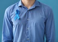 Man with symbolic blue ribbon on color background. Prostate cancer concept