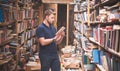 Man in a T-shirt and a beard stands in an old public library with a book in his hands Royalty Free Stock Photo