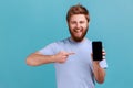 Man in T-shirt pointing finger at smartphone with black blank screen, copy space for advertisement. Royalty Free Stock Photo