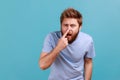 Man in T-shirt standing touching his nose, showing lie gesture, suspecting falsehood, dishonest talk