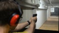 Man in tactical headphones aiming gun at target in shooting range Royalty Free Stock Photo