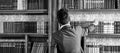 Man takes book from bookcase. Student stands in library and choose book. Guy in smart suit reads near bookcase. Study