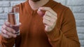 Man takes medicine with a glass of water.White pill in a young male hand