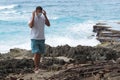 The man takes off/puts on a medical mask standing on the shore of the ocean.