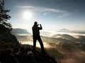 Man takes photos with phone on rock empire. Dreamy fogy mountains,