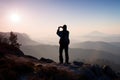 Man takes photos with smart phone on peak of rock empire. Dreamy fogy landscape, spring orange pink misty daybreak Royalty Free Stock Photo