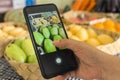 A man takes a picture of green mangoes and other produce with a cellphone at a fruit stand at a market Royalty Free Stock Photo