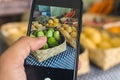 A man takes a picture of green mangoes and other produce with a cellphone at a fruit stand at a market Royalty Free Stock Photo