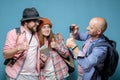 Man takes pictures of his friends with a smartphone, they smile and show thumbs up. Group of tourists travel with city