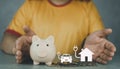 Man takes to protect on the piggy bank and paper home and car charging sustainable energy on coins in hand Royalty Free Stock Photo