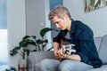 Man taking online guitar lessons via a mobile application on his phone at home sitting on the gray couch, sofa in the