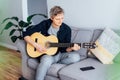 Man taking online guitar lessons via a mobile application on his phone at home sitting on the gray couch, sofa in the