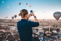 Man taking photo of beautiful landscape and balloons in Cappadocia with mobile camera, sunrise time