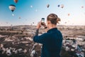 Man taking photo of beautiful landscape and balloons in Cappadocia with mobile camera, sunrise time