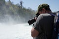 Man taking photograph of a Rhine Fall waterfall in Switzerland with a camera.