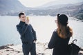 Man taking picture of his girlfriend using his smartphone near seaside and mountains Royalty Free Stock Photo