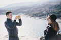 Man taking picture of his girlfriend using his smartphone near seaside and mountains Royalty Free Stock Photo