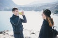 Man taking picture of his girlfriend using his smartphone near seaside and mountains Royalty Free Stock Photo