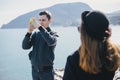 Man taking picture of his girlfriend using his smartphone near seaside and mountains Royalty Free Stock Photo