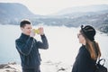 Man taking picture of his girlfriend using his smartphone near seaside and mountains Royalty Free Stock Photo