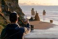 Man taking picture with mobile phone at Three Sisters rock formation by the beach in New Plymouth, New Zealand Royalty Free Stock Photo