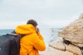 Man taking picture of woman in yellow raincoat at the cliff near sea Royalty Free Stock Photo