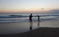 A man is taking pictures of a girl on a surfboard against the sunset. Silhouettes Royalty Free Stock Photo