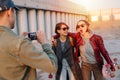 Man taking pictures of two young happy short-haired women with skateboards