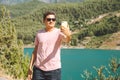 Man taking selfie on mobile phone of mountains lake background. Traveler male having video chat on cellphone on the blue Royalty Free Stock Photo