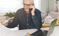 Man talking and laughing on the phone while checking work documents - Mature man working from home on the computer - Remote