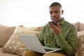 Man talking on mobile phone while using laptop on sofa in living room at comfortable home Royalty Free Stock Photo