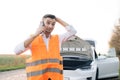 Man talking on the phone and looking at the car`s engine. young man use smartphone, stading on road near the broken car Royalty Free Stock Photo