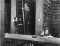 Man talking to a woman standing on a ladder in a library