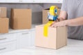 Man taping box with adhesive tape dispenser in kitchen, closeup Royalty Free Stock Photo